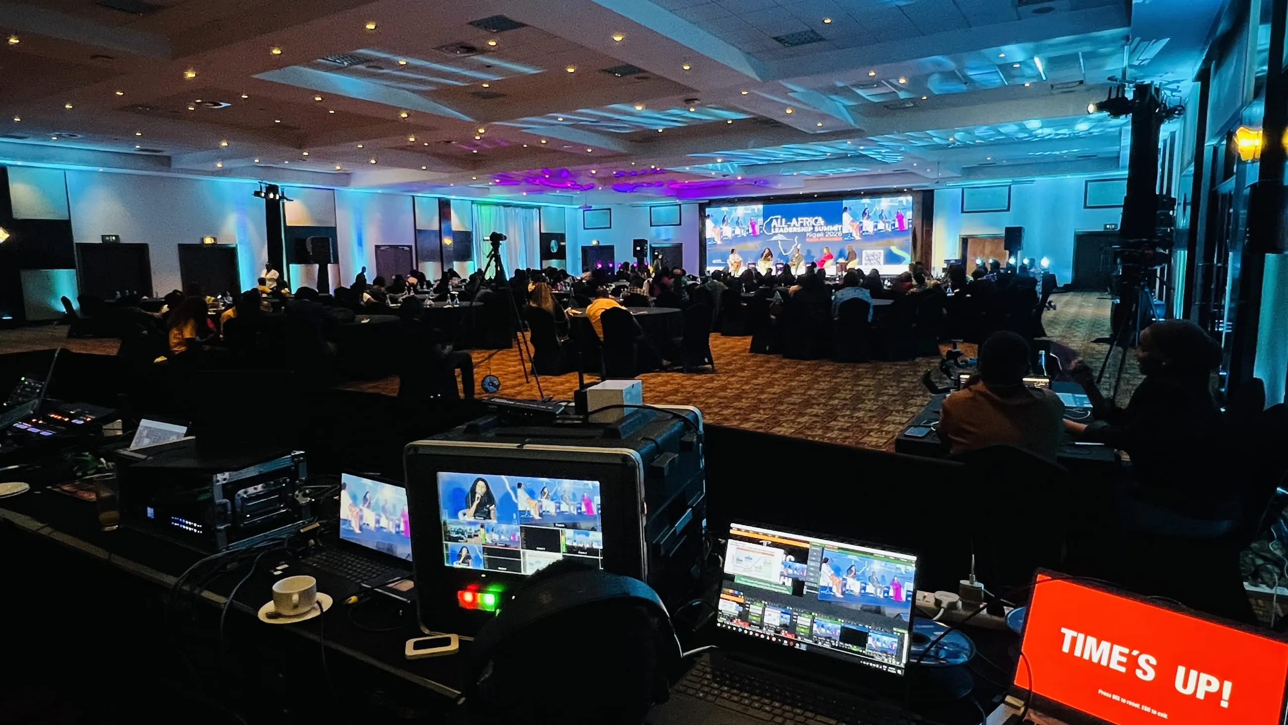 Broadcast control desk overlooking the All-Africa Leadership Summit stage in Kigali, with a large screen showing the panel discussion